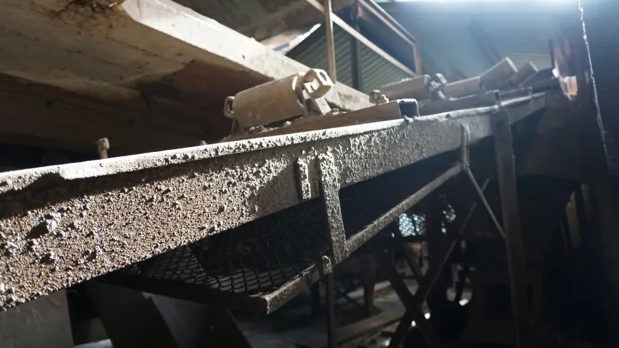 Detaillierte Aufnahme eines industriellen Förderbands mit einer texturierten Oberfläche, umgeben von rustikalem Ambiente.