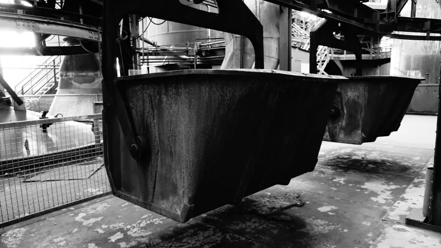 Close-up view of two industrial containers hanging in an old factory setting, showcasing their textured surfaces and a blurred background of machinery.