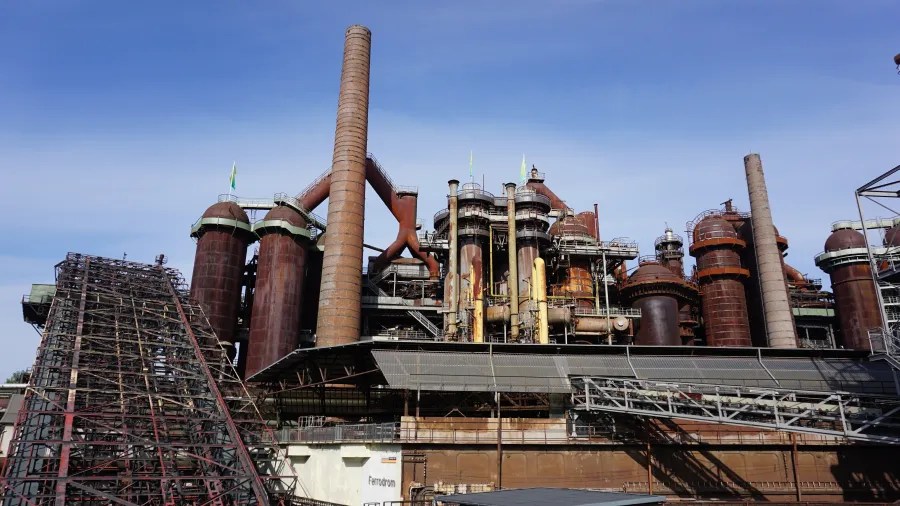 Industrieanlage mit großen Rohren und Schornsteinen unter blauem Himmel