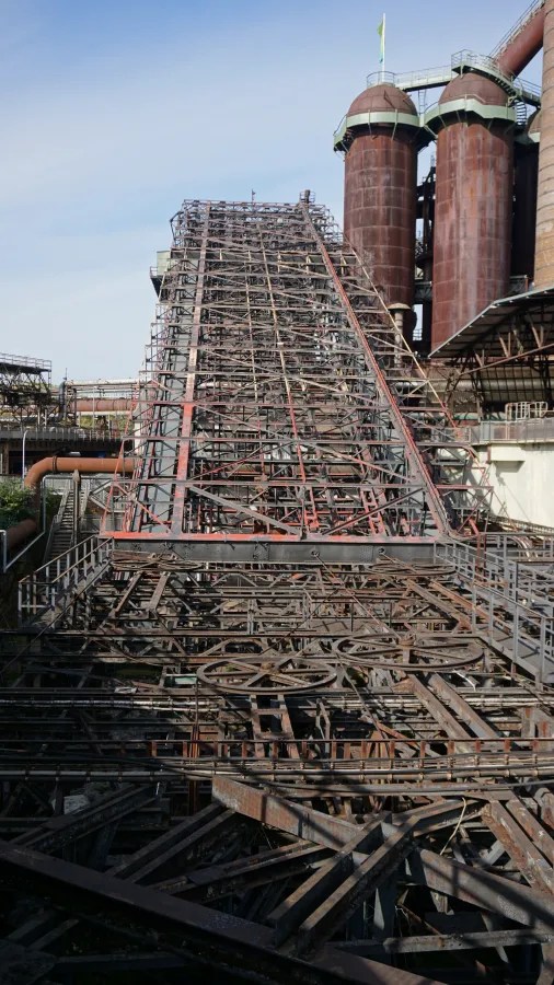 View of the Völklinger Hütte industrial site featuring a large metal conveyor structure leading up to two large cylindrical towers.
