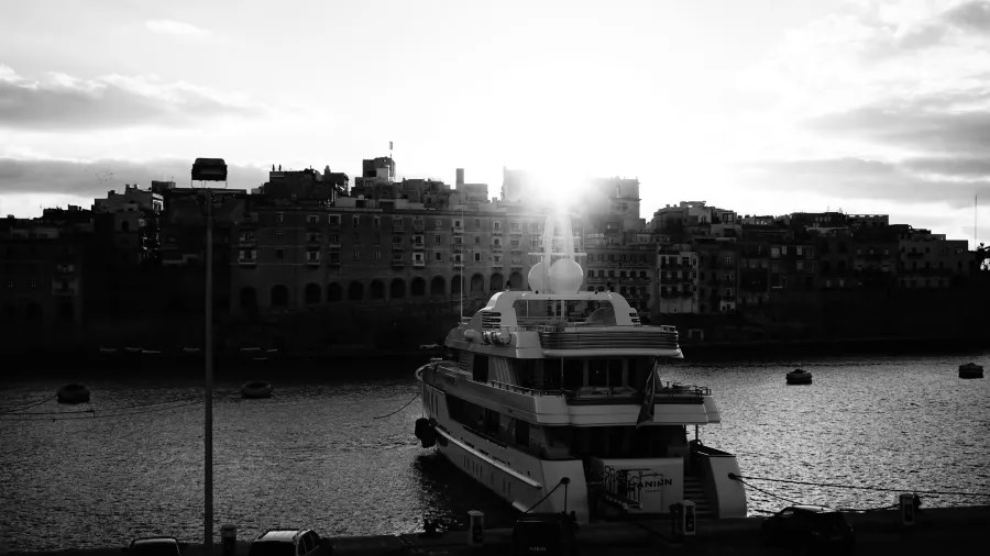 Schwarz-Weiß-Bild eines Yachts im Hafen mit der Sonne, die hinter den Gebäuden aufgeht.