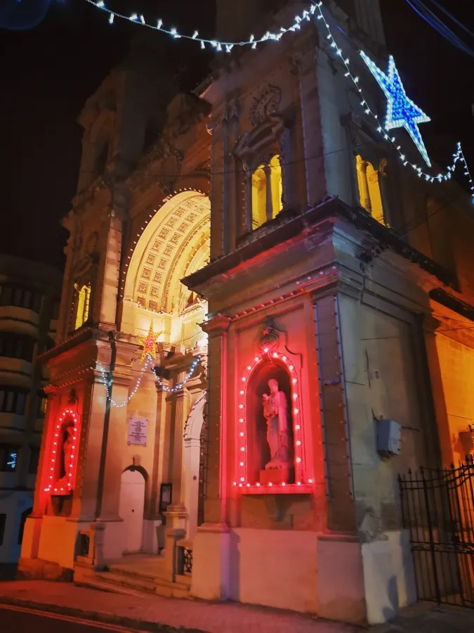 Weihnachtsbeleuchtung an einer Kirche in Malta bei Nacht, mit roten Lichtern und einem großen Stern.