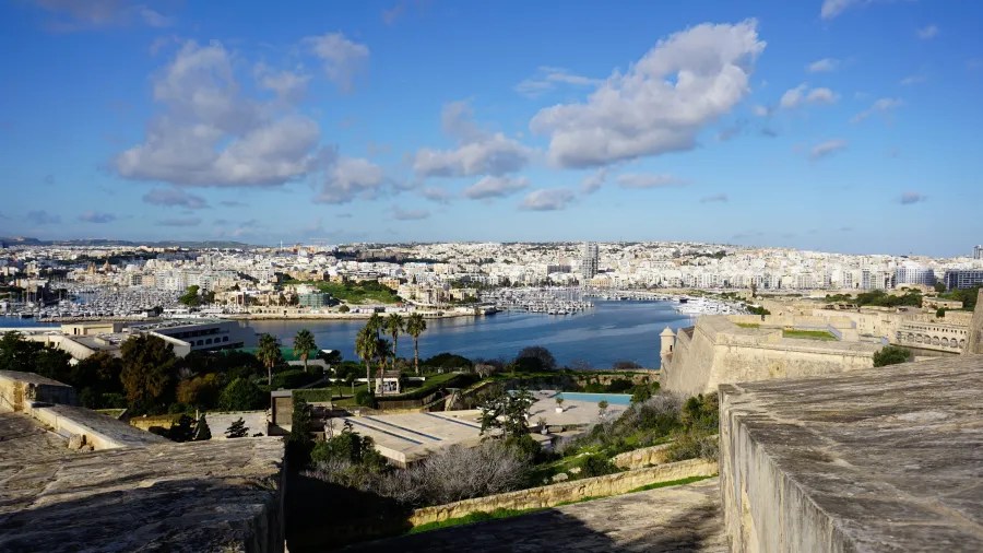Blick auf die Stadt Valletta und den Hafen von Malta, umgeben von weiß getünchten Gebäuden und weitem Himmel mit einigen Wolken.
