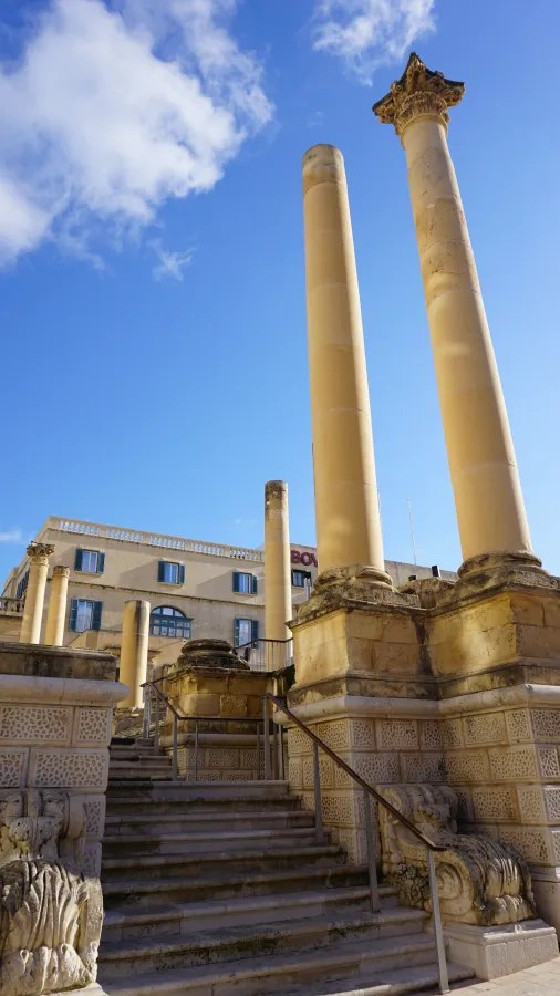 Zwei große antike Säulen vor einem historischen Bauwerk mit Wolken am Himmel.