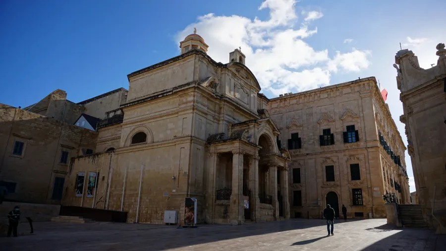 Ein historisches Gebäude in Valletta, Malta, mit einer beeindruckenden Fassade, hellen Steinwänden und einem klaren blauen Himmel im Hintergrund.