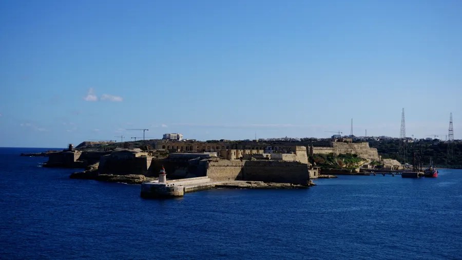 Blick auf die Küste mit Forts und Leuchtturm, unter strahlend blauem Himmel und ruhigem Wasser.