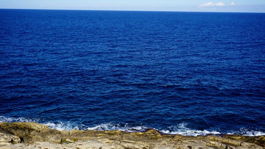 Aussicht auf das tiefblaue Mittelmeer mit sanften Wellen und einem klaren Himmel im Hintergrund.