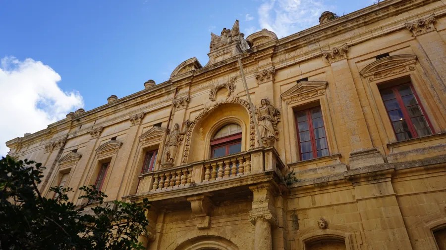 Detailaufnahme der Fassade eines historischen Gebäudes in Malta mit kunstvollen Verzierungen, Fenstern und einer Statue.