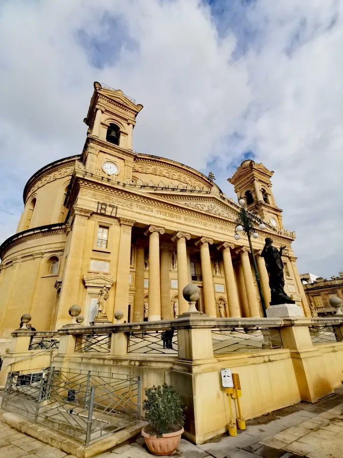 Detailansicht der beeindruckenden Rotunda von Mosta in Malta, mit Säulen und skulpturalen Elementen sowie einer Statue vor der Fassade.