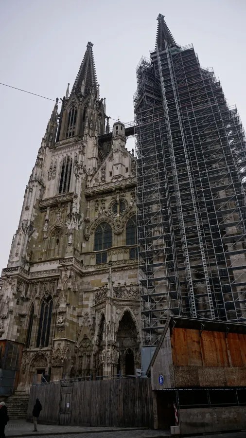 Der Regensburger Dom, beeindruckende gotische Architektur, teilweise mit Baugerüsten für Restaurierungsarbeiten, vor einem grauen Himmel.