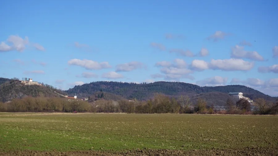 Weite Landschaft mit Feldern und sanften Hügeln unter einem blauen Himmel mit weißen Wolken.