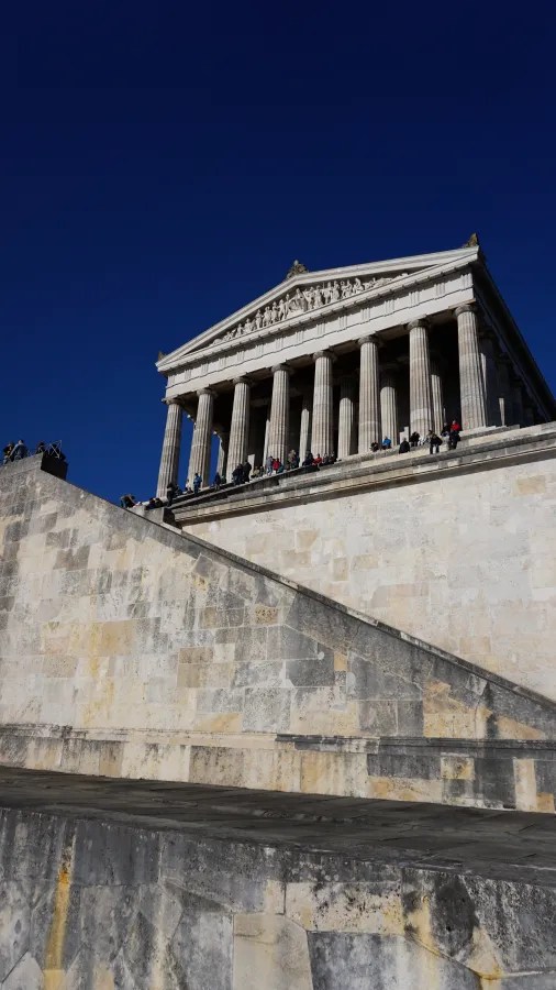 Blick auf die Walhalla mit klassischen Säulen und Treppen, im Hintergrund strahlend blauer Himmel.
