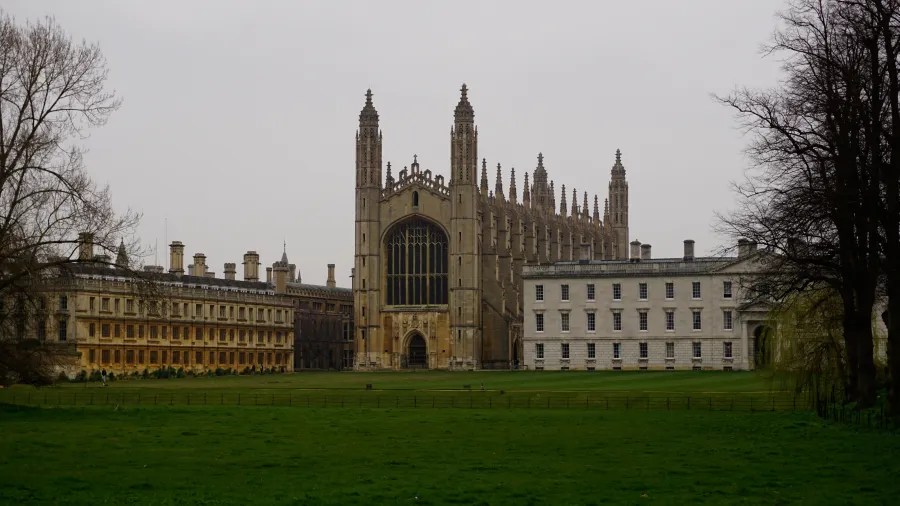 Das Bild zeigt die beeindruckende King's College Chapel in Cambridge, umgeben von historischer Architektur und einer grünen Rasenfläche unter einem grauen Himmel.