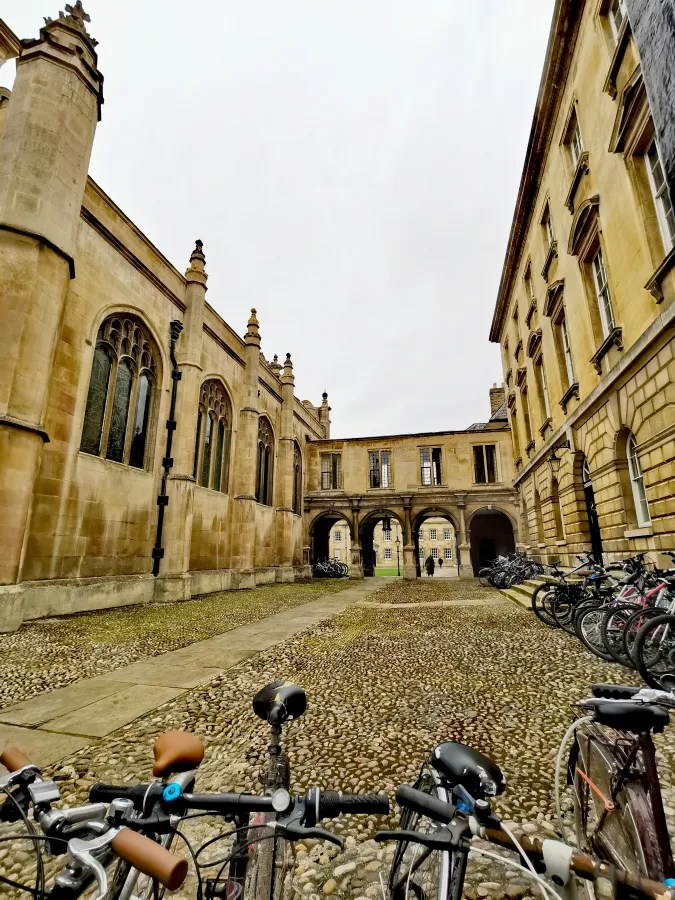 Blick auf einen gepflasterten Innenhof der Universität Cambridge, umgeben von historischen Gebäuden und Fahrrädern.