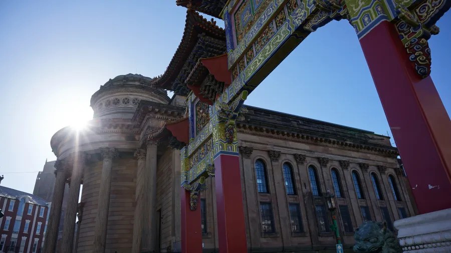 Ansicht eines historischen Gebäudes in der Nähe eines chinesischen Torbogens mit Sonnenlicht, das von hinten strahlt.