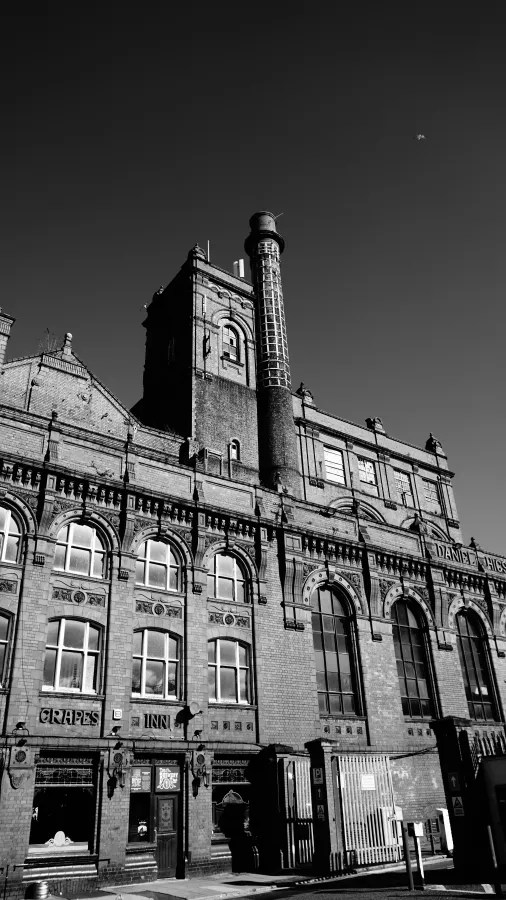 Historisches Gebäude mit hoher Fassade und Schornstein, aufgenommen im Schwarz-Weiß-Stil.