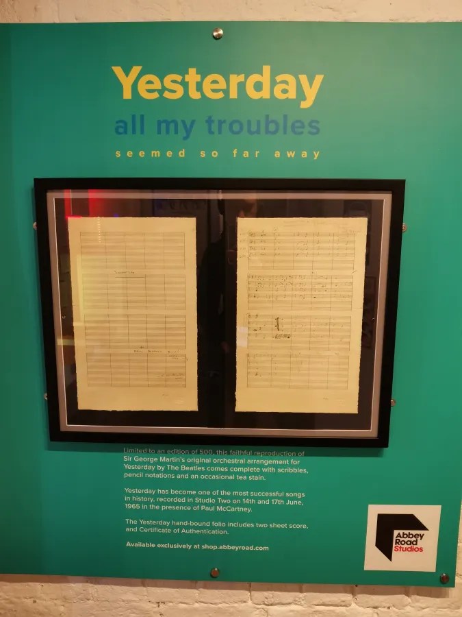 Ein gerahmtes Stück handschriftlicher Partitur von 'Yesterday' der Beatles, umgeben von einer Informationswand über die musikalische Bedeutung und Authentizität.