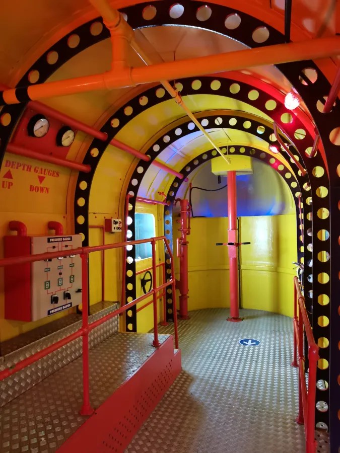 Innenansicht eines farbenfrohen Tauchgeräts mit bunten Rohren, Druckmessgeräten und einem gestreiften Boden.