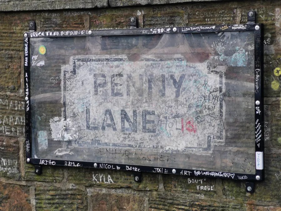 Schild mit der Aufschrift "Penny Lane", umgeben von Graffiti und Markierungen auf einer Mauer.