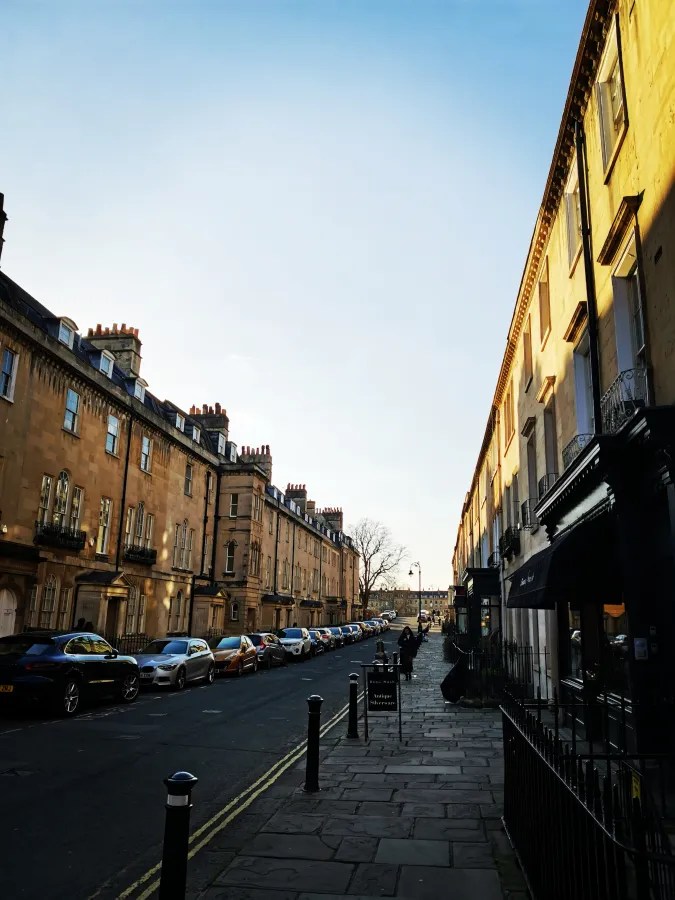 Eine ruhige Straße mit historischen Gebäuden auf beiden Seiten, parkenden Autos und einem klaren Himmel.