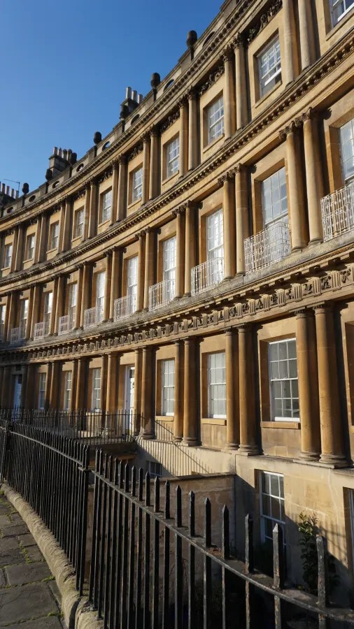 Fassade eines historischen, gebogenen Gebäudes mit Säulen und Fenstern unter klarem blauen Himmel.