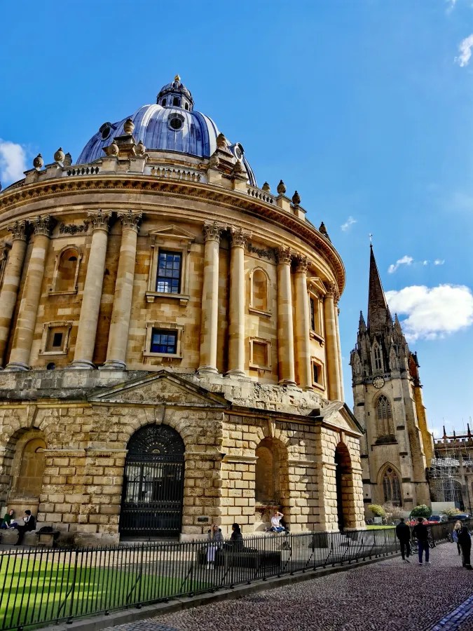 Eine Ansicht des Bodleian Library mit der beeindruckenden Kuppel und angrenzenden Gebäuden in Oxford, unter einem blauen Himmel.