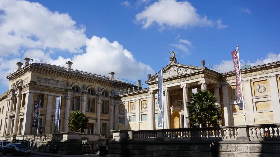 Eine historische Gebäudeansicht mit beeindruckender Architektur, Säulen und Fahnen, umgeben von einem hellen Himmel mit Wolken.
