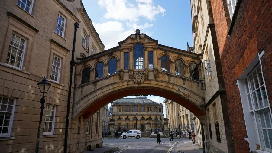 Ein historischer Bogen über einer Straße in Oxford, umgeben von alten Gebäuden und einem blauen Himmel mit wenigen Wolken.