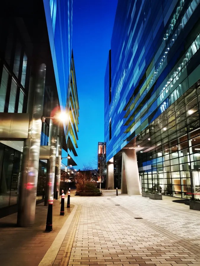 Moderne Architektur in einer urbanen Umgebung bei Nacht, mit gläsernen Fassaden und einem klaren blauen Himmel.