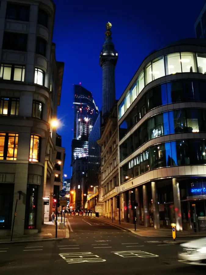 Nachtansicht einer Stadtstraße mit modernen und historischen Gebäuden bei Dämmerung.