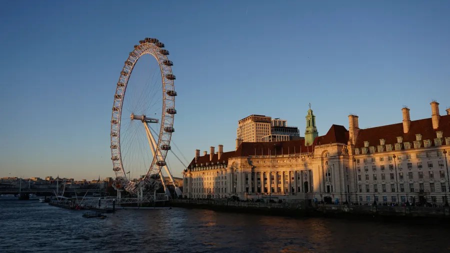 Das London Eye mit der Themse im Vordergrund und historische Gebäude im Hintergrund bei Sonnenuntergang.