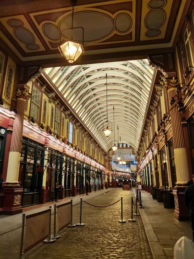 Ein historischer Marktplatz mit eleganter, gewölbter Decke und nostalgischen Laternenbeleuchtung. Die Straßen sind mit Steinen gepflastert, und es gibt Absperrungen, die den Zugang regeln.