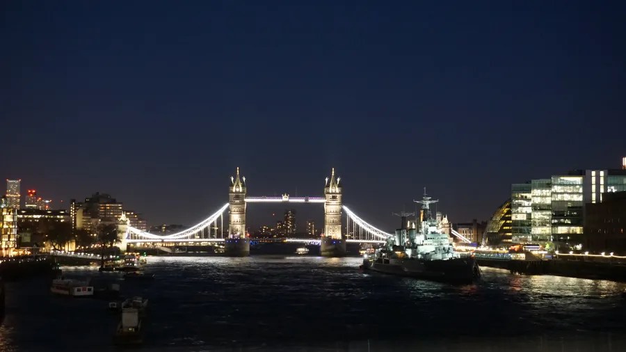 Die Tower Bridge bei Nacht, beleuchtet, mit einem Schiff im Vordergrund auf der Themse.