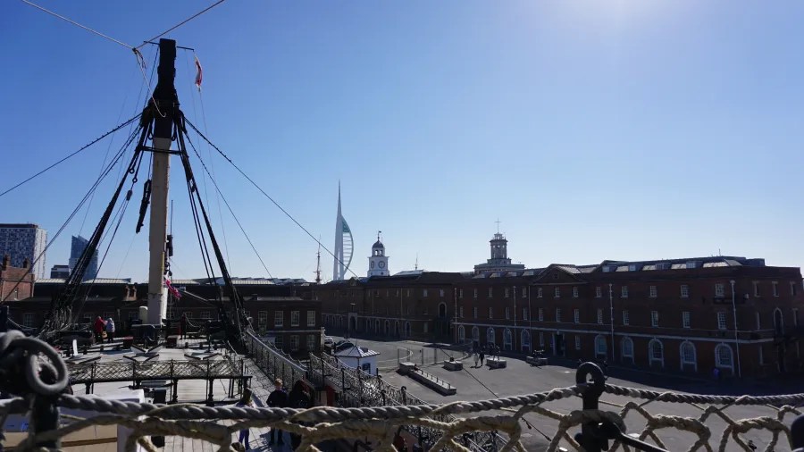 Blick von einem Schiffsoberdeck auf die Hafenstadt mit historischen Gebäuden und moderner Architektur unter einem klaren blauen Himmel.
