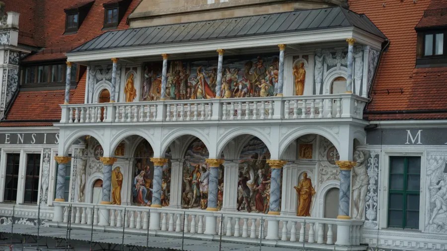 Fassade eines historischen Gebäudes mit bunten Wandmalereien und einem offenen Balkon mit kunstvollen Säulen.