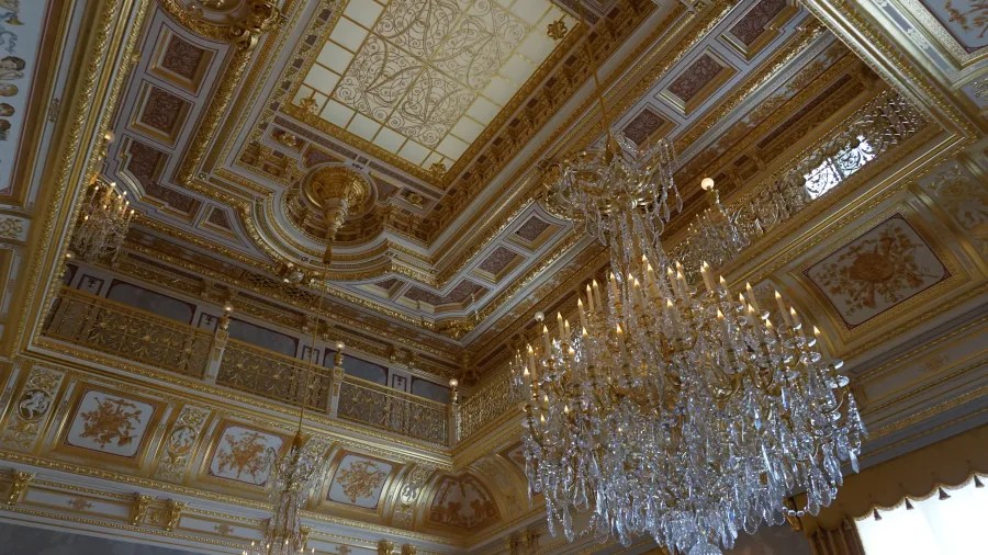 Prunkvoller Deckenbereich mit goldenen Verzierungen und einem großen Kristallkronleuchter.