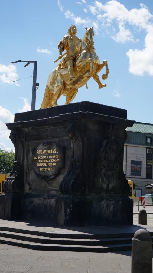 Reiterstatue des Friedrich Augustus I. auf einem monumentalen Sockel, in goldenem Farbton, unter blauem Himmel mit wenigen Wolken.