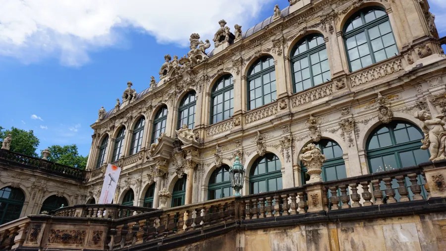 Die prächtige Fassade eines historischen Gebäudes mit kunstvollen Verzierungen und großen Fenstern unter einem blauen Himmel.