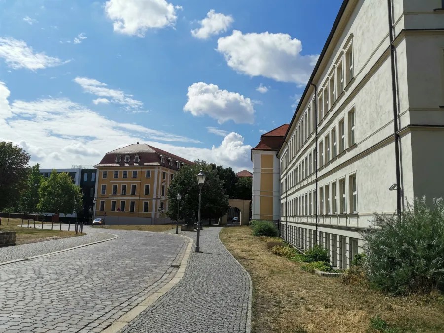 Eine gepflasterte Straße mit Gebäuden auf beiden Seiten und einem blauen Himmel mit Wolken.