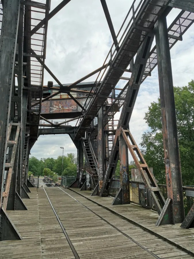 Eisenbahnbrücke mit rustikalem, gealtertem Metallrahmen und Holzplanken, unterbewachsen mit Graffiti, unter einem bewölkten Himmel.