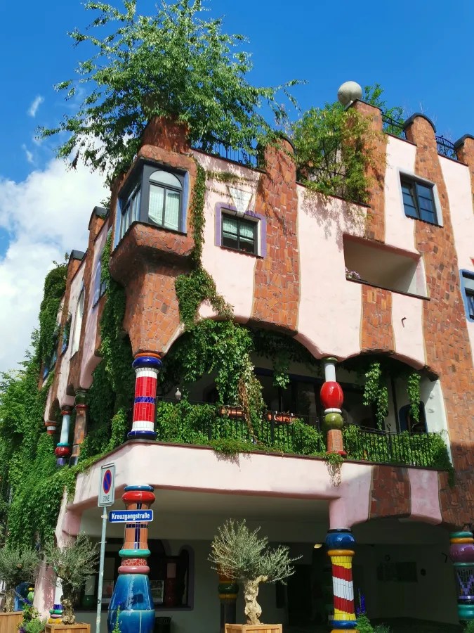 Buntes und kreatives Gebäude mit vielen Pflanzen und detailreicher Fassade, begleitet von einem blauen Himmel.