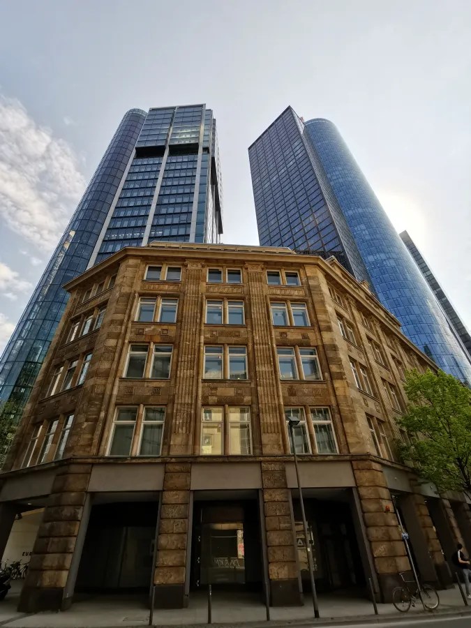 Blick auf ein historisches Gebäude im Vordergrund, umgeben von modernen Wolkenkratzern in einer städtischen Umgebung.
