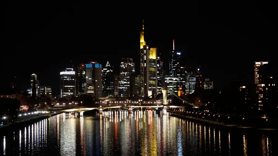 Beleuchtete Skyline von Frankfurt am Main bei Nacht, reflektiert im Fluss Main.