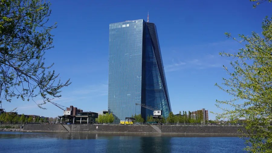 Das Hauptgebäude der Europäischen Zentralbank am Ufer eines Gewässers mit blauem Himmel im Hintergrund.