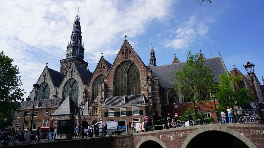Blick auf eine historische Kirche mit markanter Fassade und hohen Türmen, umgeben von Bäumen und einer belebten Straße.
