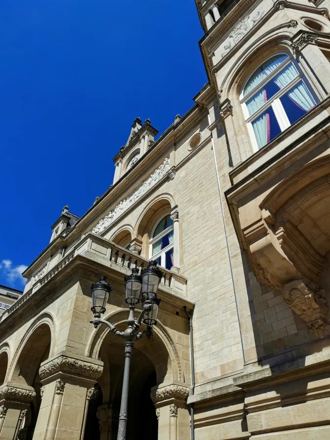 Blick auf die Fassade eines historischen Gebäudes mit hohen Fenstern und einer Uhr, unter strahlend blauem Himmel.