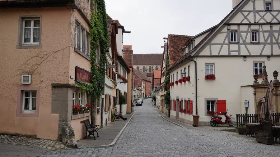 Eine malerische Straße in einer historischen Stadt, gesäumt von traditionellen Häusern mit Blumenkästen und einem gepflasterten Weg.