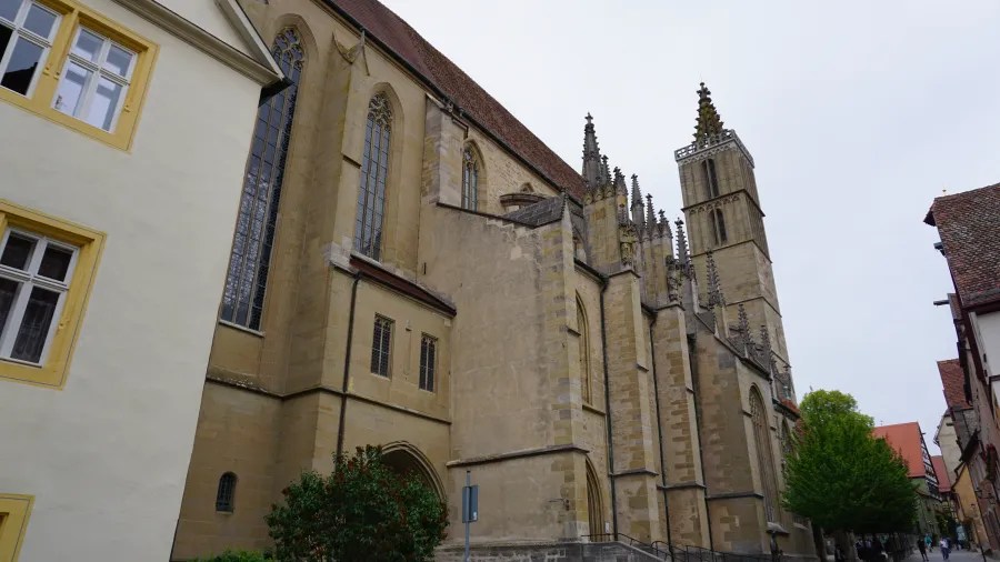 Seitenansicht einer historischen Kirche mit hohen Türmen und gotischen Elementen, umgeben von alten Gebäuden und Bäumen.