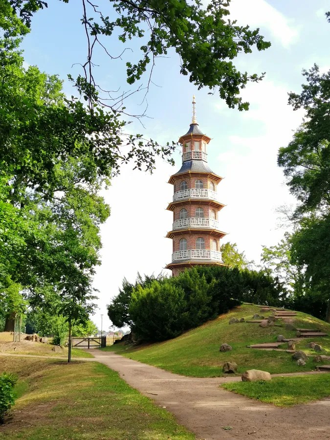 Eine mehrstöckige Pagode in einem Park, umgeben von Bäumen und einem Pfad im Vordergrund.