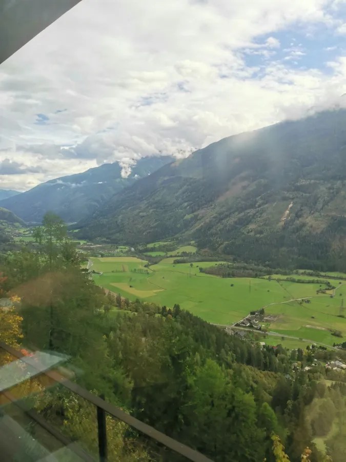Blick auf eine grüne Landschaft mit Bergen im Hintergrund und bewolktem Himmel.